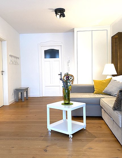 Gemütliches Wohnzimmer mit Holzboden, weißen Wänden und einem grauen Sofa