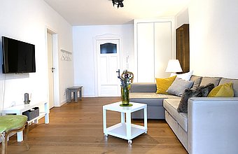 Gemütliches Wohnzimmer mit Holzboden, weißen Wänden und einem grauen Sofa